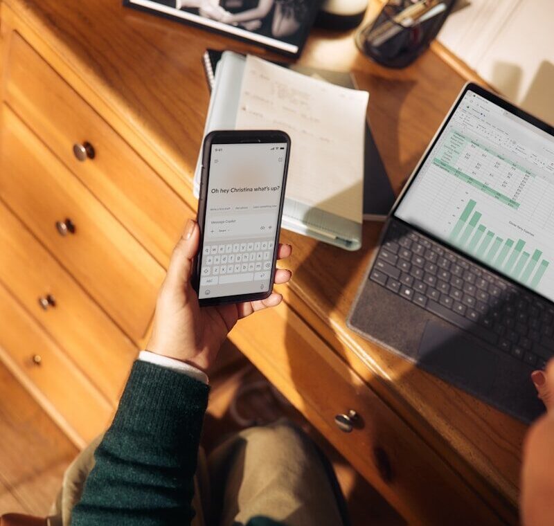 Person holding phone near laptop and tablet on desk